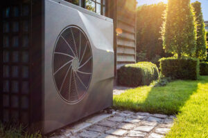 Your HVAC System Can Enhance Sleep. Close-up of black full inverter heat pump outside in the garden, near wooden pool house on a sunny day. Lens flare on the image.