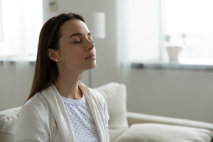 5 Tips to Improve Your Home’s Indoor Air Quality (IAQ) This Winter. A woman sitting inside on her couch breathing in clean air.