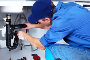 Professional plumber repairing a pip under a sink in a home.